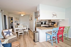 Una cocina compacta con muebles blancos, un refrigerador de acero inoxidable y una pequeña isla con sillas coloridas.