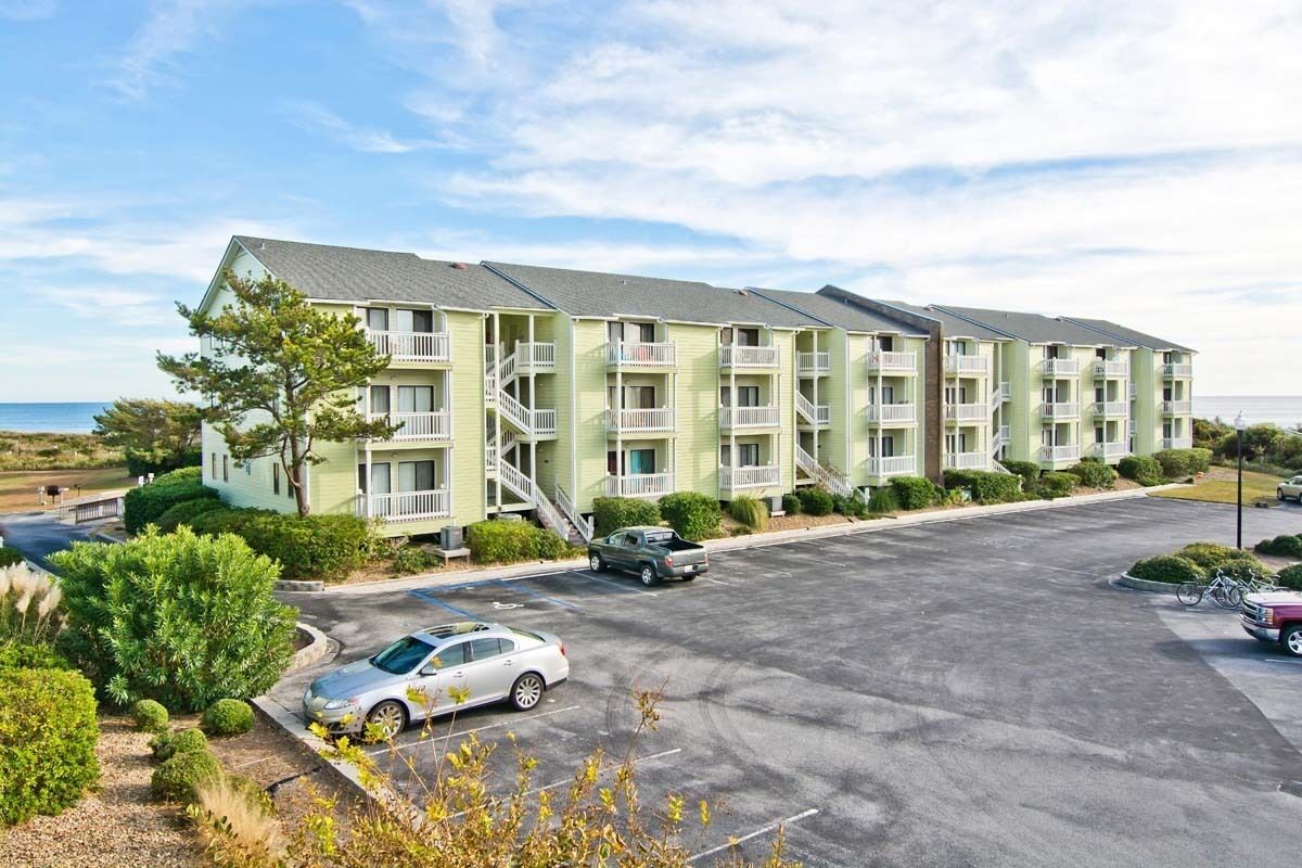 A multi-story motel with balconies, a parking lot, and a view of the ocean.