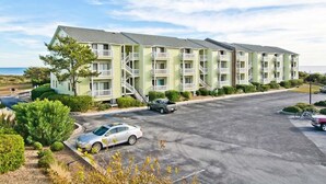 A multi-story motel with balconies, a parking lot, and a view of the ocean. - Pebble Beach A-204, Oceanfront Condo in Emerald Isle, NC! (Emerald Isle)