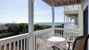 A covered balcony with white railings, a table, and two chairs. - Pebble Beach A-204, Oceanfront Condo in Emerald Isle, NC! (Emerald Isle)