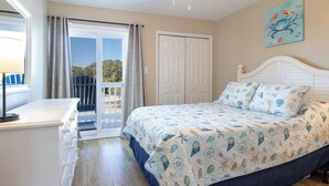 A bedroom with a bed, a dresser, a ceiling fan, a door, and a view of the outdoors. - Pebble Beach A-207, Oceanfront Condo in Emerald Isle, NC! (Emerald Isle)