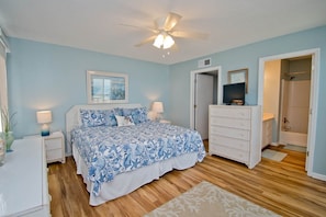 A bedroom with a bed, nightstands, a dresser, a ceiling fan, and a door leading to a bathroom. - Pebble Beach A-301, Oceanfront Condo in Emerald Isle, NC! (Emerald Isle)