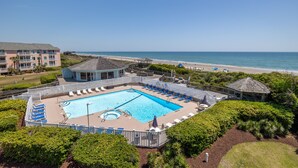 A pool area with a view of the beach, surrounded by greenery and a building with a balcony. - Pebble Beach A-304, Oceanfront Condo in Emerald Isle, NC! (Emerald Isle)
