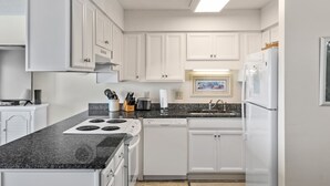 A modern kitchen with white cabinets, a granite countertop, a dishwasher, and a refrigerator. - Pebble Beach A-304, Oceanfront Condo in Emerald Isle, NC! (Emerald Isle)