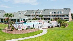 Ein Hotel mit mehreren Balkonen, einem Schwimmbad und einem gepflegten Rasen.