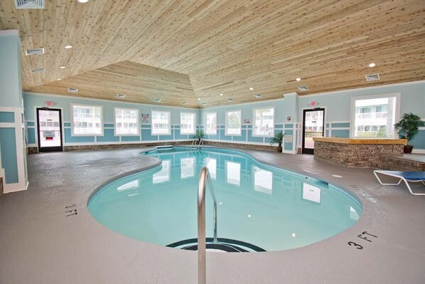 An indoor swimming pool with a wooden ceiling, clear signage, and a stone accent wall.
