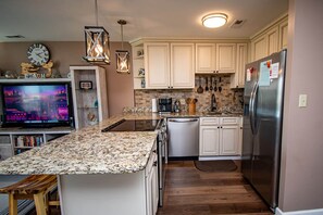 A modern kitchen with white cabinets, granite countertops, a stainless steel refrigerator, and a built-in oven.