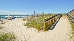 A sandy beach with a wooden boardwalk, beach umbrellas, and people relaxing. - Pebble Beach D-202, Oceanfront Condo in Emerald Isle, NC! (Emerald Isle)