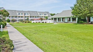 A hotel with multiple buildings, a well-maintained lawn, and a clear sky. - Pebble Beach 1-110, Oceanside Condo in Emerald Isle, NC! (Emerald Isle)