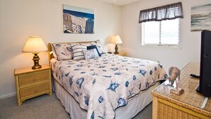 Une chambre à coucher comprenant un lit, deux lampes de chevet, un ventilateur de plafond, un téléviseur et des œuvres d’art accrochées aux murs.