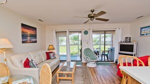 A spacious living room with a sofa, chairs, a coffee table, and a television. - Pebble Beach 1-110, Oceanside Condo in Emerald Isle, NC! (Emerald Isle)
