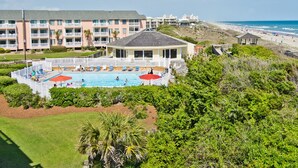 Et hotel med poolområde, omgivet af frodig vegetation og udsigt til stranden.
