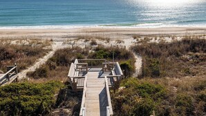 A beach view with a wooden boardwalk leading to a structure with benches. - Pelican Perch, Oceanfront House in Emerald Isle, NC! (Emerald Isle)