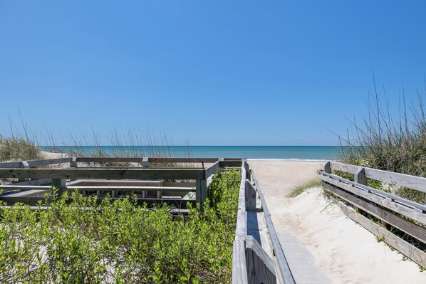 A wooden boardwalk leading to a sandy beach with a clear blue sky.