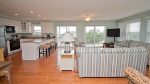 A spacious living area with a kitchen, a dining area with bar stools, a striped sofa, a television, and a ceiling fan.