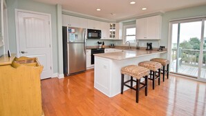 A kitchen with white cabinets, a stainless steel refrigerator, a microwave, and a large island with bar stools.