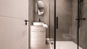 A modern bathroom with a glass shower enclosure, a white sink, and a mirror above it. - The Battersea Scenery - Elegant 2bdr Flat (London)