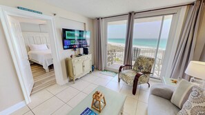 Une chambre d’hôtel avec un lit, une télévision, un balcon donnant sur la plage et une chaise.