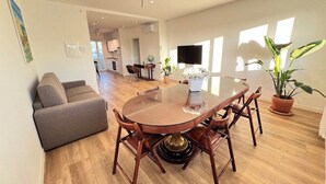 A spacious living area with a round wooden dining table, a sofa, and a potted plant.