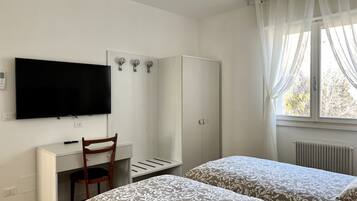 Ein Hotelzimmer mit Bett, Schreibtisch mit Stuhl, Kleiderschrank, Fernseher und einem Fenster mit Vorhängen.