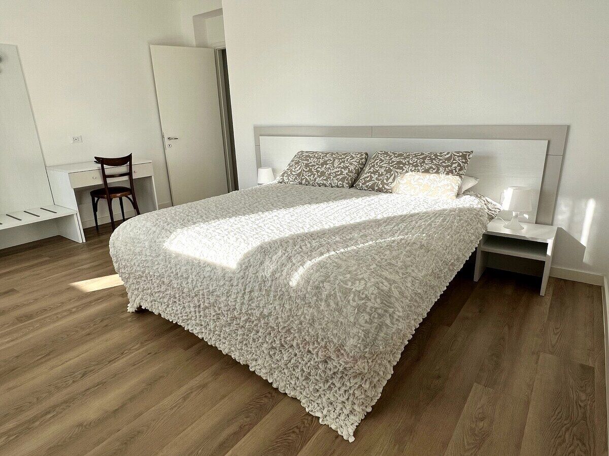A bedroom with a large bed, a nightstand, a chair, and a wardrobe.