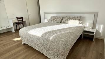 A bedroom with a large bed, a nightstand, a chair, and a wardrobe.