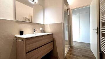 A modern bathroom with a wooden vanity, a large mirror, and a glass shower enclosure.