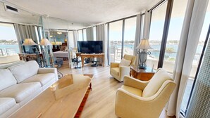 A spacious living area with a sofa, armchairs, a TV, and a balcony with a view of the sea. - East Pass Towers 304 is a Stunning 3 bedroom with Pass Views and recent upgrades (Destin)