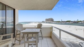 Un balcon avec une table et des chaises, donnant sur une plage et un port de plaisance.