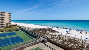 A beach view with a tennis court, beach umbrellas, and a white sandy beach. - HSR 402 is a Luxury 2 BR - Completely Renovated and stunning in its decor (Destin)