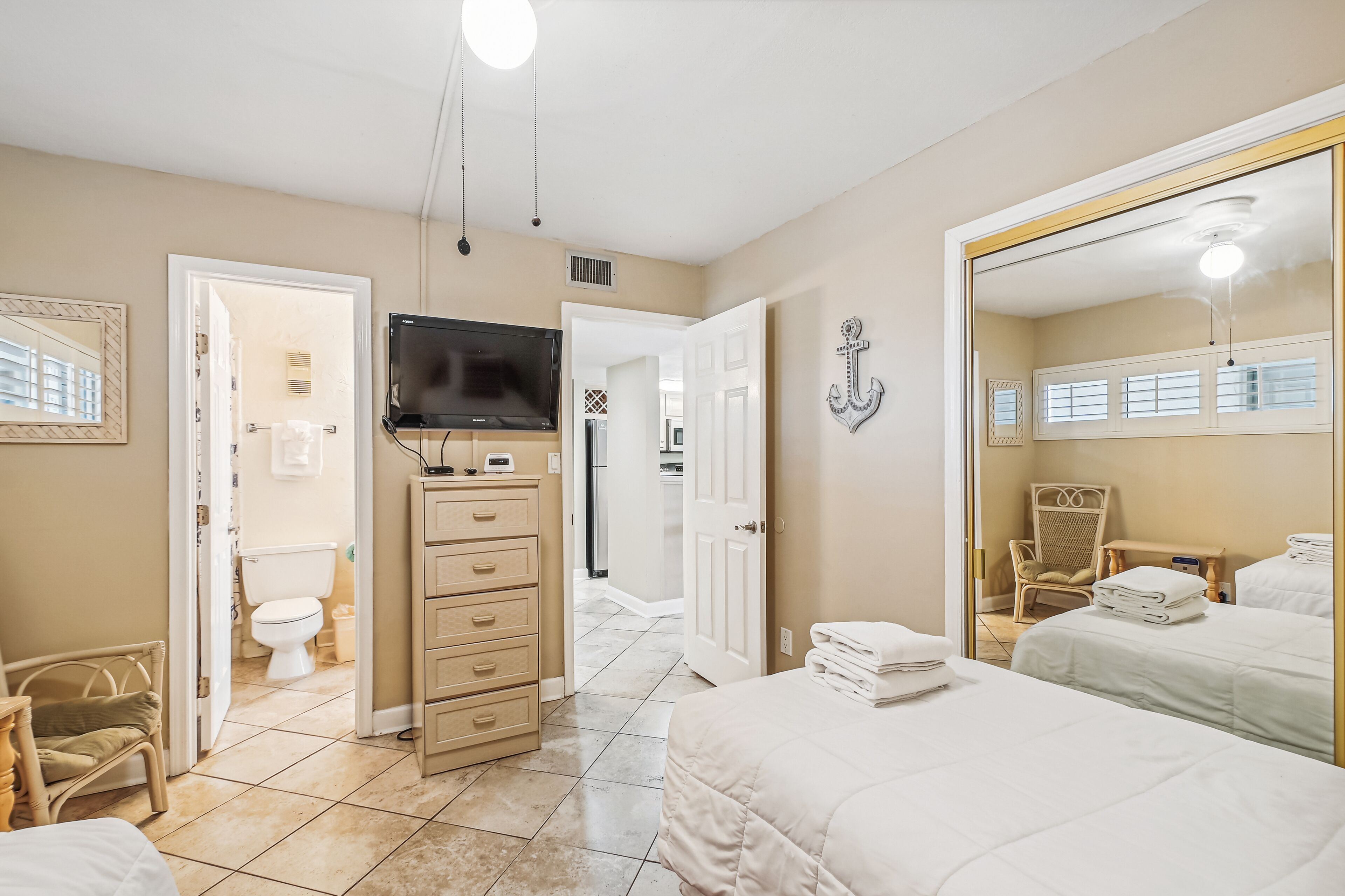 A hotel room with a bed, a TV, a dresser, a chair, and a bathroom visible through an open door.