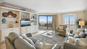 A spacious living room with a large flat-screen TV, comfortable seating, and a view of the ocean through a sliding glass door. - 🏖️Beach Front 2BR Inlet Reef 102-Free Seasonal Beach Service for 2🏖️ (Destin)