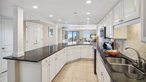 A modern kitchen with white cabinetry, black countertops, and a large island. - 🏖️Beach Front 2BR Inlet Reef 102-Free Seasonal Beach Service for 2🏖️ (Destin)