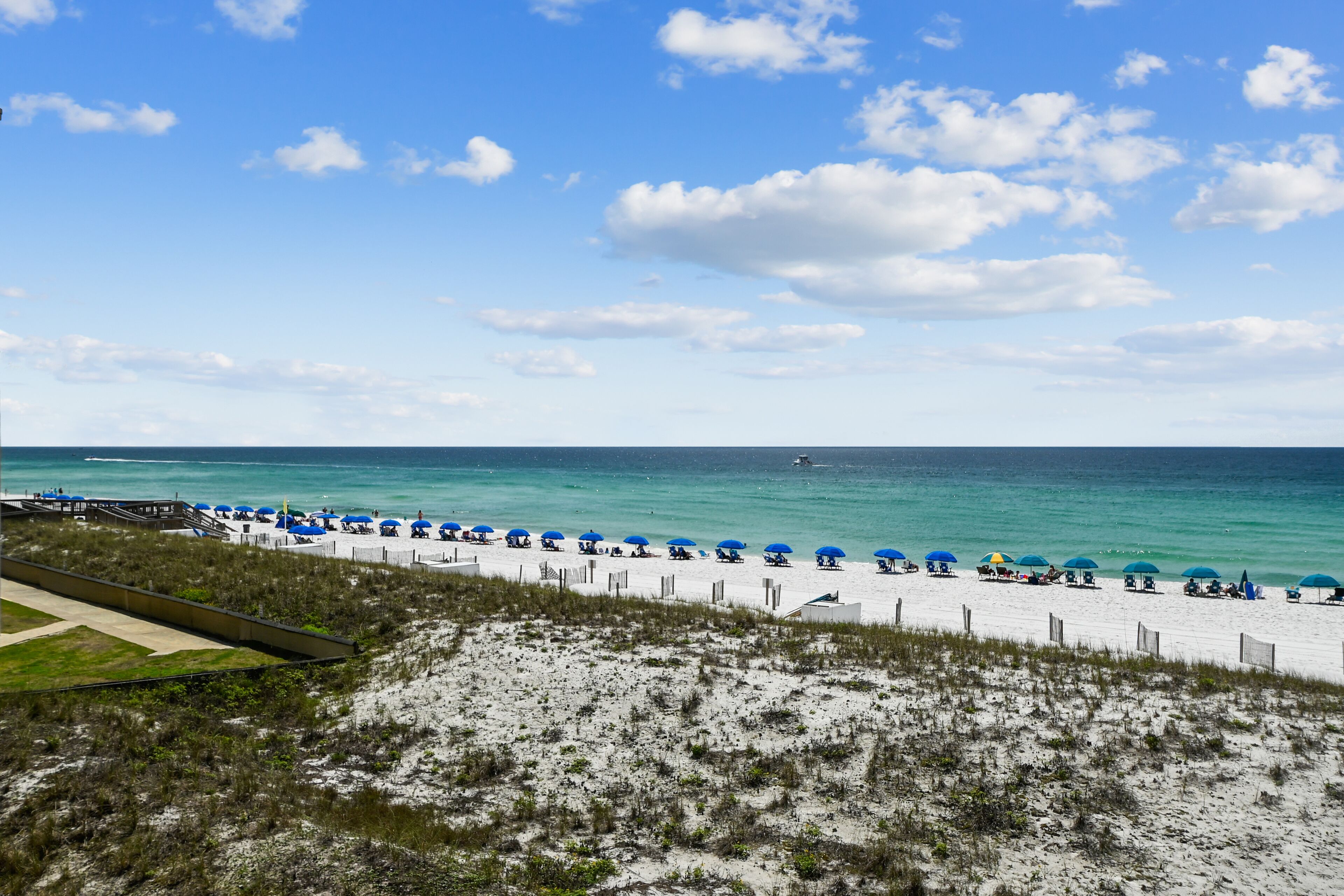 A beach with white sand, blue umbrellas, and a clear sky.