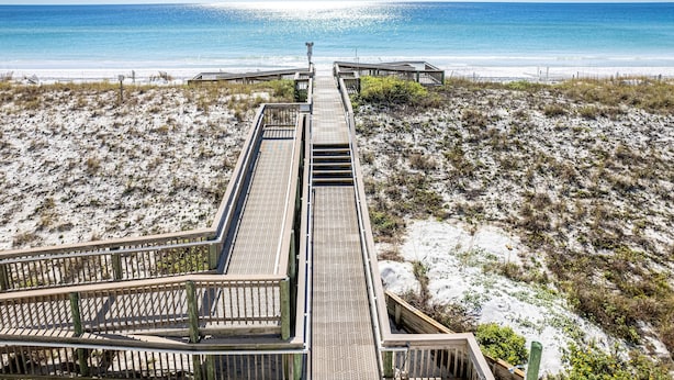 Une promenade en bois qui mène à une plage offrant une vue dégagée sur l’océan.