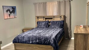 A bedroom with a wooden bed, a ceiling fan, a nightstand, and a small wooden table. - Relax with your family in this newly renovated home away from home.  (Orange)