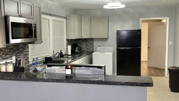 A modern kitchen with grey cabinets, a black refrigerator, and a microwave. - Relax with your family in this newly renovated home away from home.  (Orange)