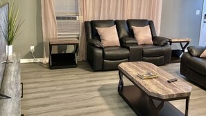 A modern living room with a sectional sofa, a coffee table, and a side table. - Relax with your family in this newly renovated home away from home.  (Orange)