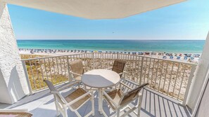 Un balcon donnant sur une plage, avec une balustrade blanche et une table entourée de chaises.
