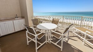 Varanda com mesa e cadeiras brancas, pequena área de cozinha e vista para a praia.
