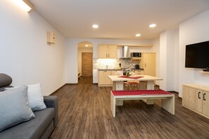 A modern living room with a grey sofa, wooden flooring, a dining table with red and white tablecloth, and a kitchen in the background. - Apartments Goldhorn Kingdom  - One Bedroom Apartment with Balcony (B) (Bohinj)