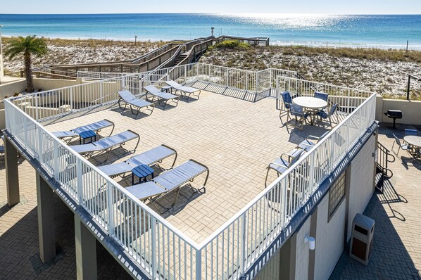 Une terrasse sur le toit, dotée de chaises longues, d’une table et de chaises, offrant une vue sur la plage.