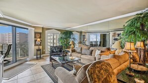 A spacious living room with a large sofa, a coffee table, and a balcony with a view of buildings.