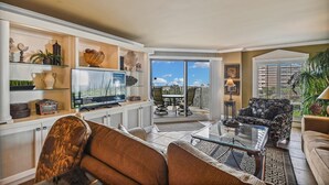 A living room with a television, a sofa, a coffee table, and a balcony with outdoor furniture.