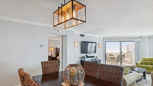 Una sala moderna con una mesa de comedor de madera oscura, sillas tejidas, una lámpara colgante y un ventanal con vistas a la ciudad.