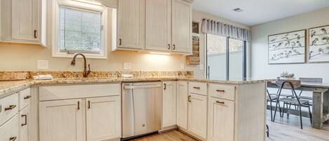 A kitchen with light-colored cabinets, a built-in dishwasher, and a window with blinds.