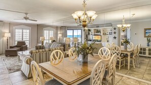 Un vaste espace dédié à la salle à manger, avec une grande table en bois et des chaises assorties, un lustre, et une vue sur l’océan grâce à de grandes fenêtres.