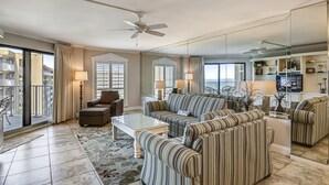 Un salon spacieux avec un grand canapé, des fauteuils et une table basse. Il y a un balcon avec une chaise et une lampe.