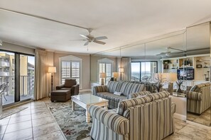 A spacious living room with a large sofa, armchairs, and a coffee table. There is a balcony with a chair and a lamp. - IR 516 Sunset Views to marvel at in this 2 BR on the beach side of Holiday Isle (Destin)