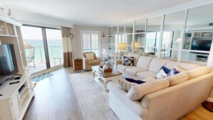 Een ruime woonkamer met een grote bank, een televisie en een balkon met uitzicht op zee.
